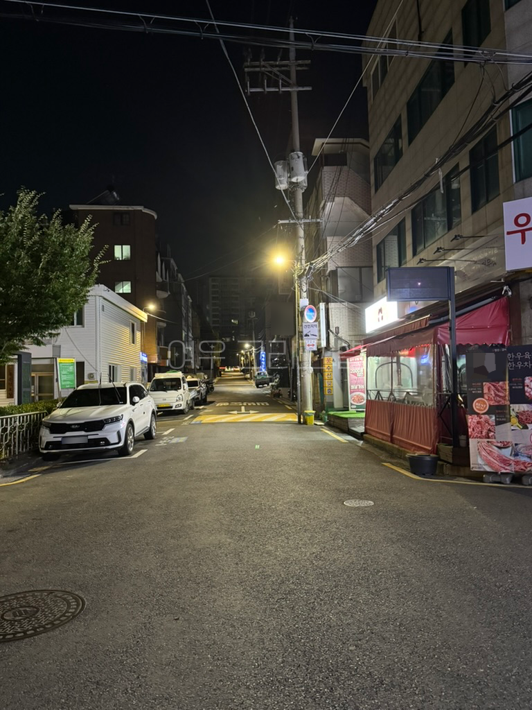 아스팔트로 포장된 골목길. 왼쪽에는 차들이 주차되어 있고, 오른쪽으로는 가게들이 있다. 앞에는 과속방지턱이 보인다.